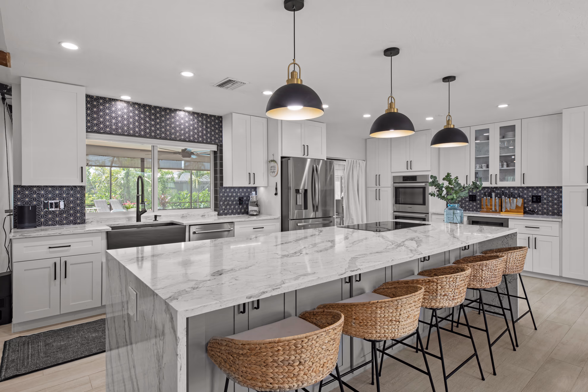Remodeled Fort Myers kitchen with a marble waterfall island, white shaker cabinets, and black pendant lights by HomeWorks Construction