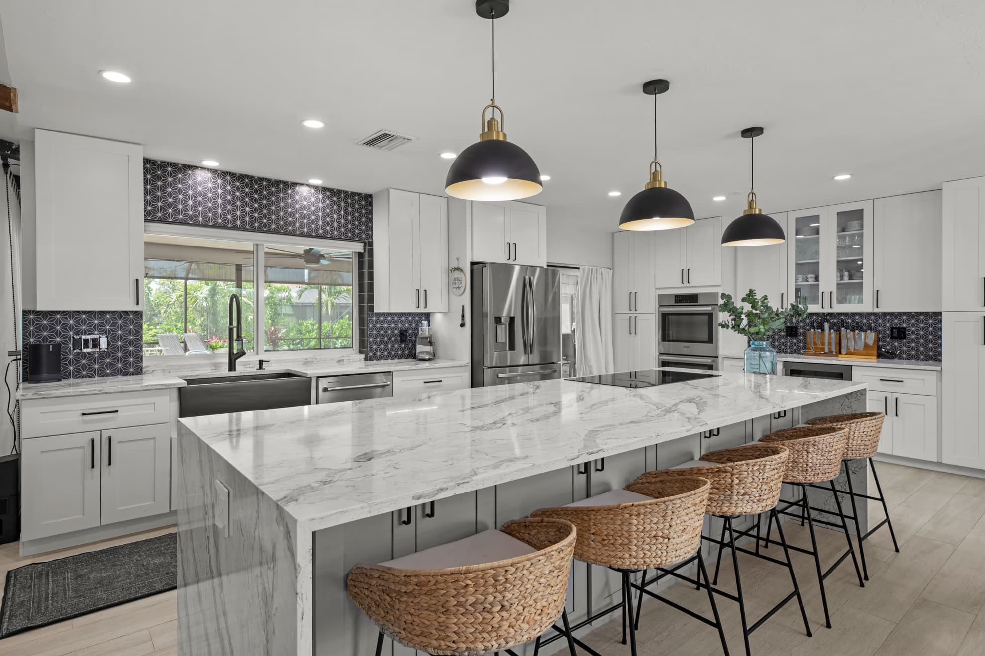 Remodeled Fort Myers kitchen with a marble waterfall island, white shaker cabinets, and black pendant lights by HomeWorks Construction